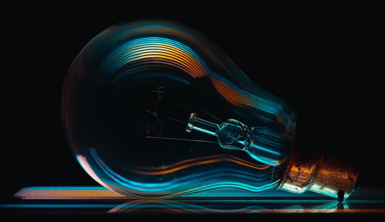 Creative close-up of a light bulb with colorful reflections against a black backdrop, symbolizing ideas and innovation.